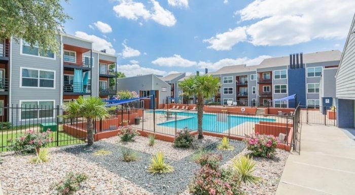 A pool surrounded by a gravel garden area with plants and trees at Infinity on the Landing Apartments, Euless, Texas