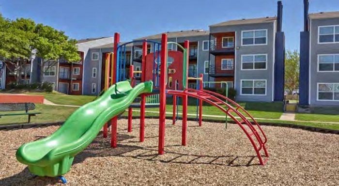 A green slide in a playground with red and grey play equipment at Infinity on the Landing Apartments, Euless, TX, 76040