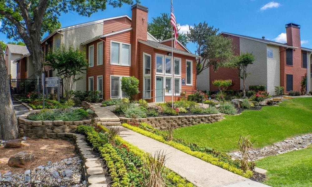 A house with a flag on the front porch is surrounded by a garden at Infinity on the Oaks Apartments, Dallas, TX