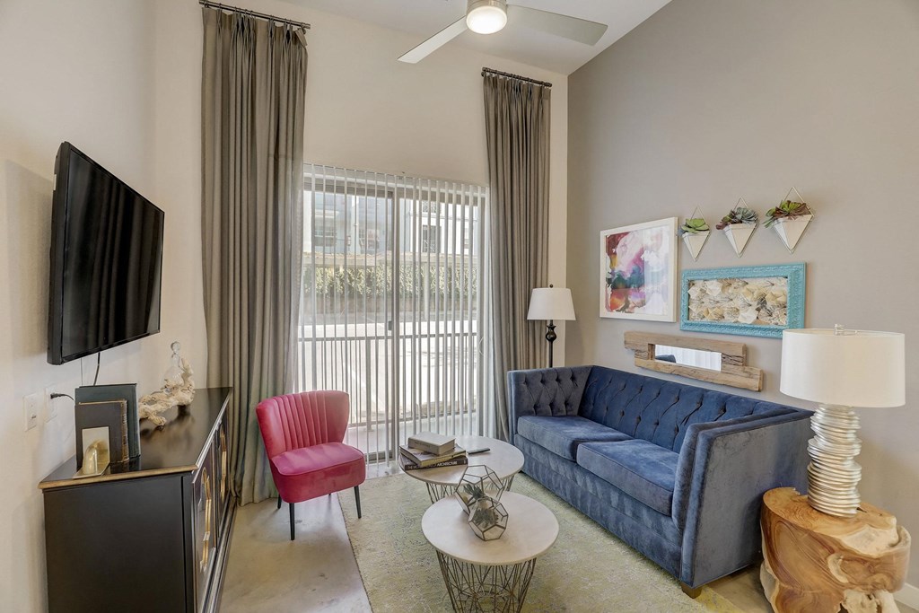 A living room with a blue couch, a red chair, and a television at Infinity on the Point Apartments, Dallas