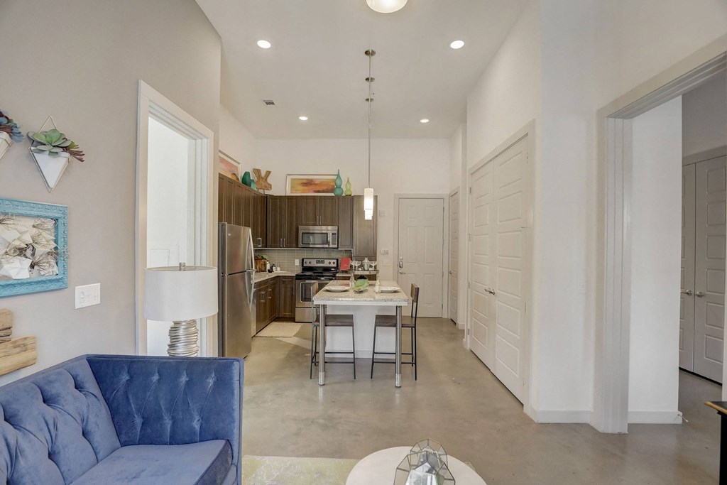 A blue couch is in the foreground of a modern kitchen and dining area at Infinity on the Point Apartments, Texas, 75243