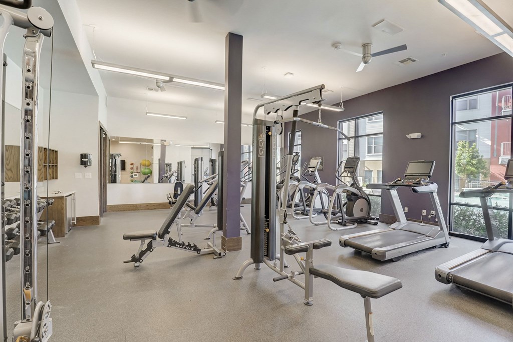 A spacious gym with a variety of equipment including treadmills, weight machines, and a bench press at Infinity on the Point Apartments, Texas