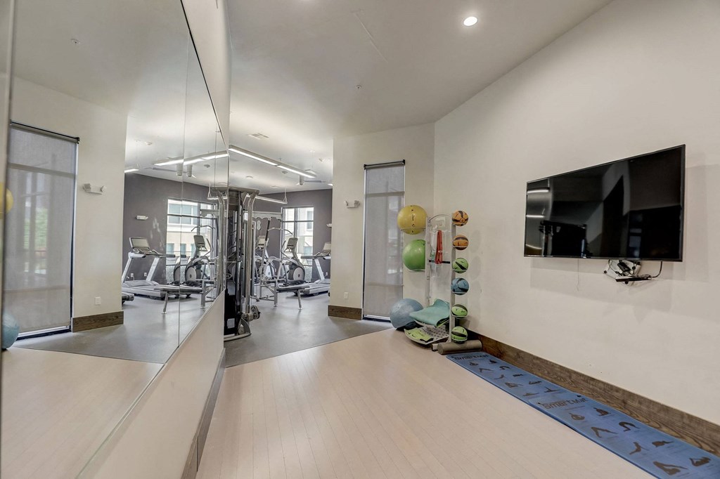 A spacious gym with a mirror on the wall and various exercise equipment at Infinity on the Point Apartments, Dallas, Texas