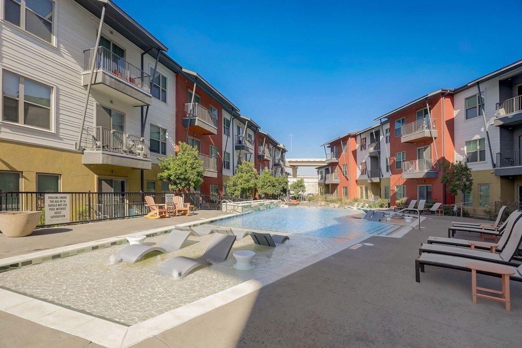 A pool surrounded by lounge chairs and apartment buildings at Infinity on the Point Apartments, Dallas, Texas