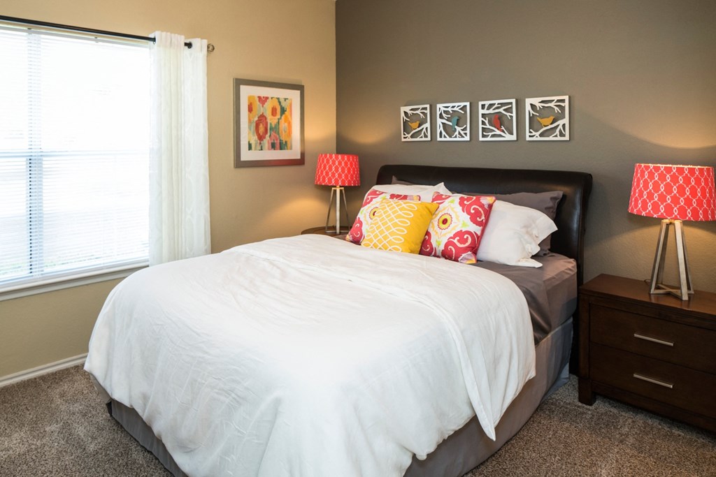 A bedroom with a white bed and two red and white lamps.