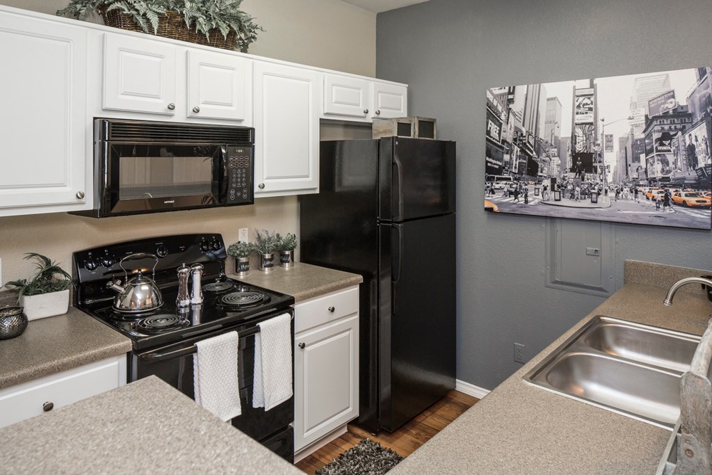 A black refrigerator sits in a kitchen with white cabinets.