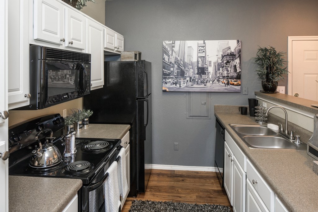 A black and white photo of a city street is hanging on the wall above a black refrigerator in a kitchen.