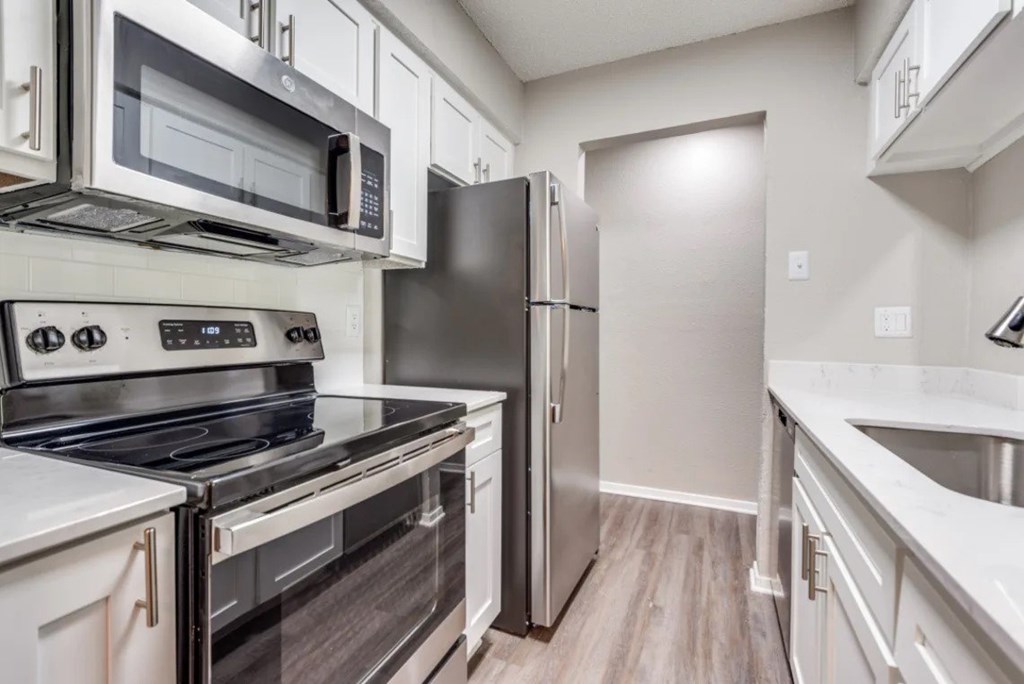 A kitchen with a stove, oven, microwave, refrigerator, and sink at Infinity on the Oaks Apartments, Texas