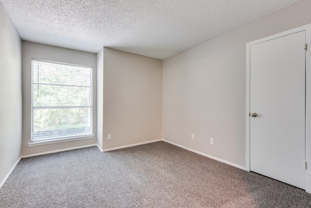 A room with a carpeted floor, a window with blinds, and a white door at Infinity on the Oaks Apartments, Dallas, TX
