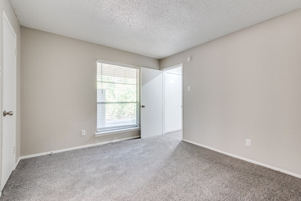 A room with a carpeted floor and a window with blinds at Infinity on the Oaks Apartments, Dallas 75231