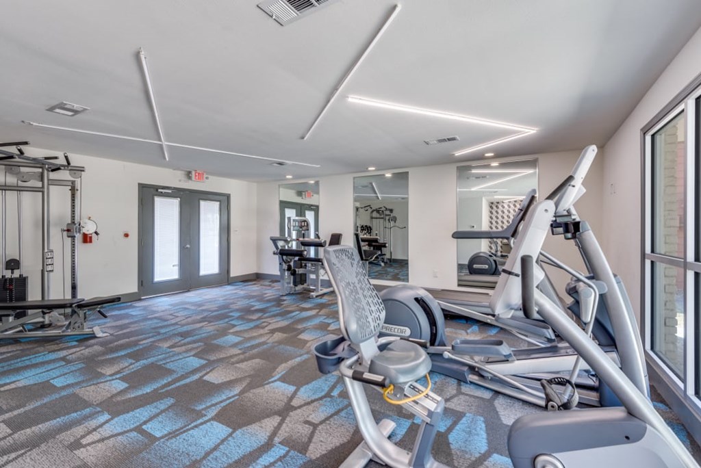 A gym with a treadmill, elliptical machines, and other exercise equipment at Infinity on the Oaks Apartments, Dallas