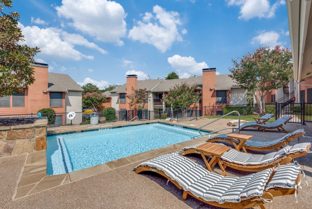 A pool surrounded by lounge chairs and a fence at Infinity on the Oaks Apartments, Texas