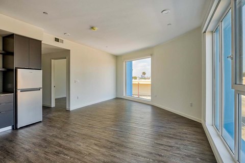 A spacious room with wooden flooring and a refrigerator in the corner.