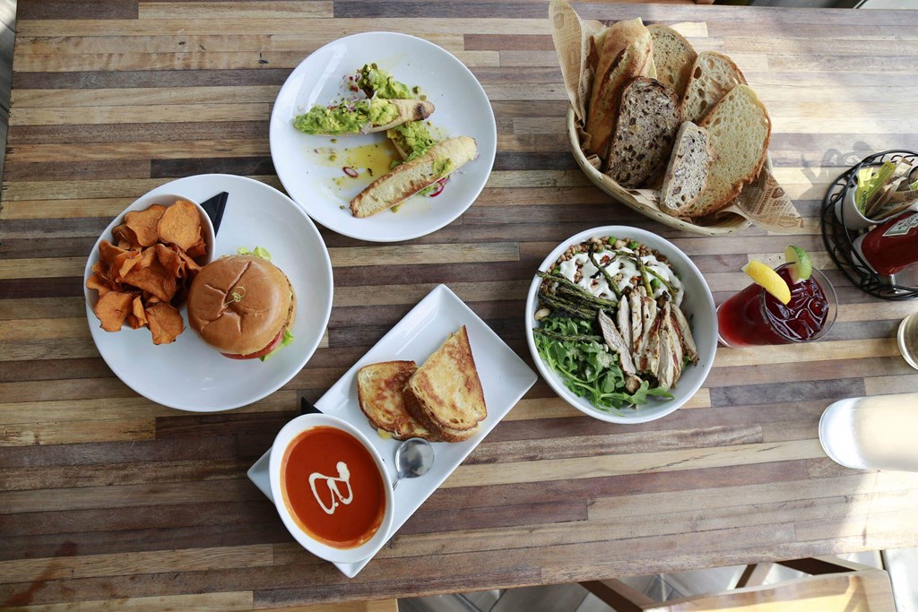 A wooden table with a variety of food including a sandwich, salad, and soup. at The Geffen, Los Angeles, CA