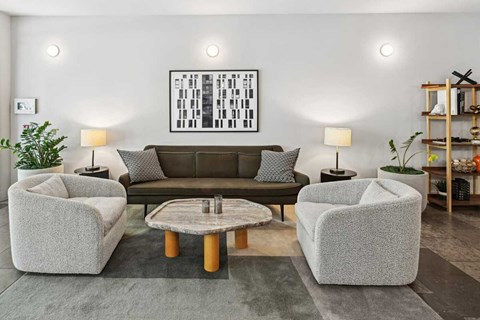 A living room with a grey sofa, two grey armchairs, a coffee table, and a painting on the wall.