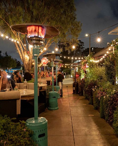 A restaurant with tables and chairs under umbrellas and string lights.at The Wilson, Santa Monica, CA
