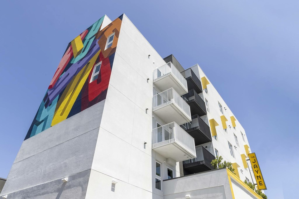 A white building with a colorful mural on the side and a yellow sign on the top right.