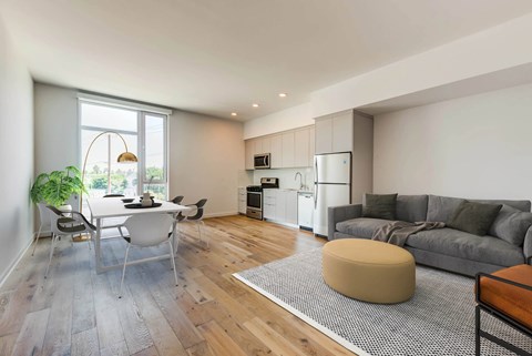 A modern kitchen with a dining table and chairs is adjacent to a living room with a grey couch and a bean bag.