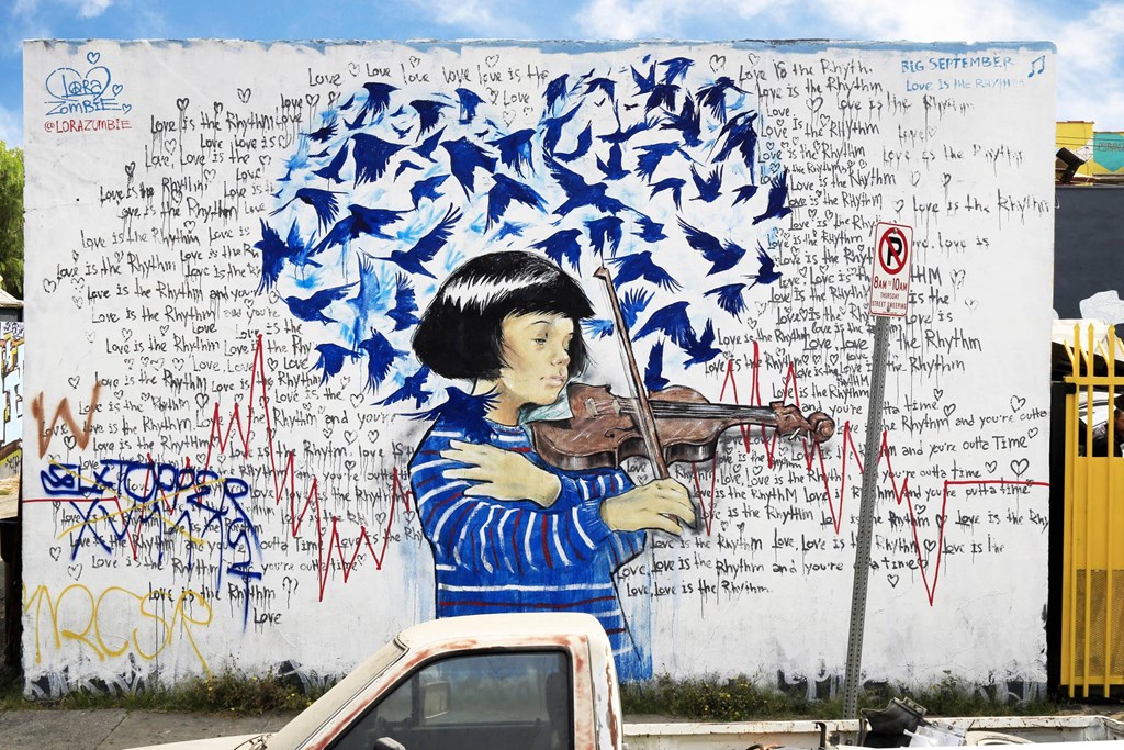 A mural of a woman playing a violin is covered in graffiti.at 5263 W Adams, Los Angeles, CA