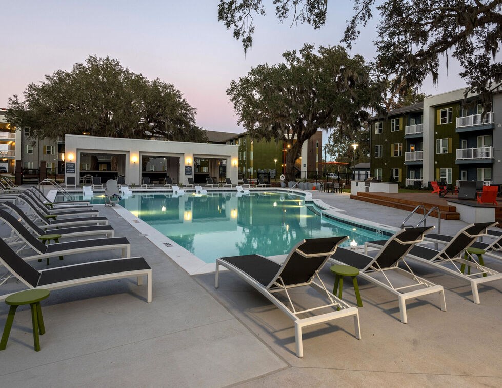 A poolside area with lounge chairs and a building in the background. at Mariner Grove, Savannah, GA