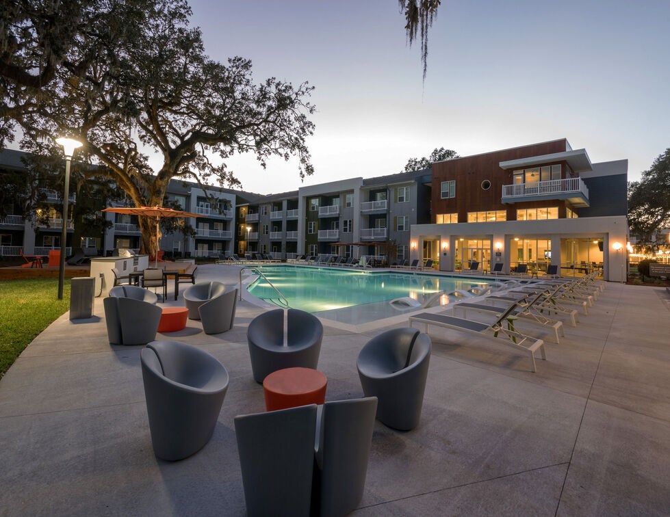 A modern outdoor pool area with lounge chairs and a building in the background. at Mariner Grove, Savannah, GA