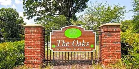 A sign for "The Oaks Apartment Homes for Active Seniors" is displayed in front of a brick wall.