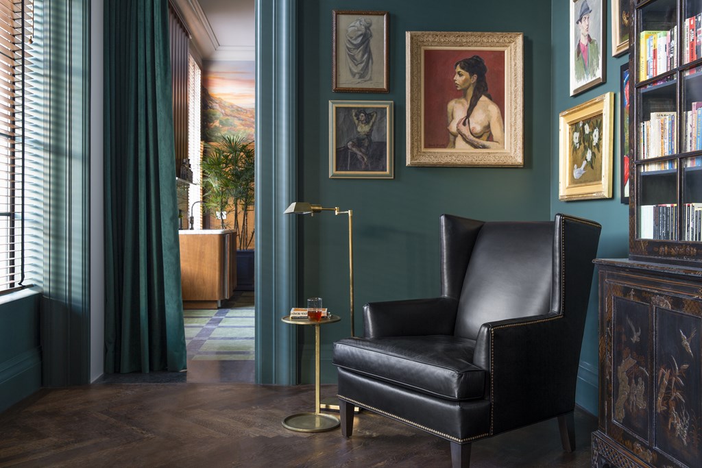 A black leather chair sits in front of a green wall with a painting of a woman on it.