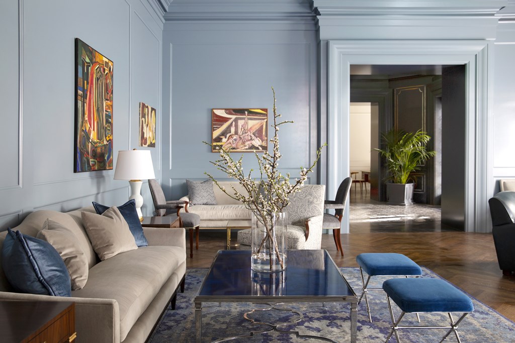 A living room with a beige couch, a glass coffee table, and a blue rug.