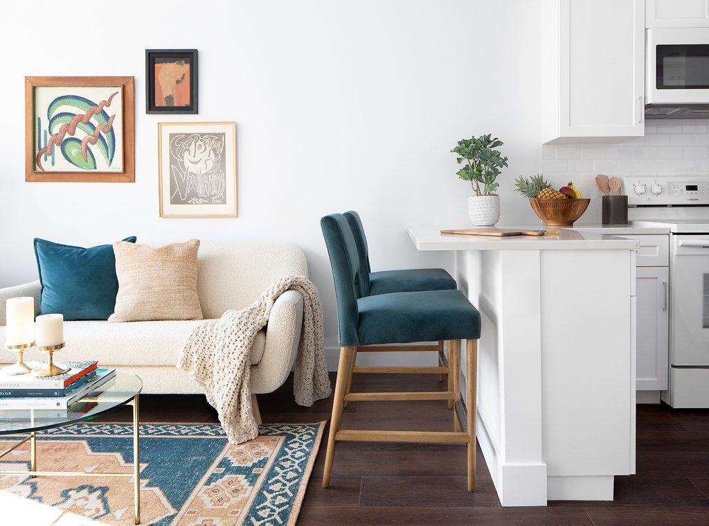 A white couch with a blue pillow and a white blanket is in front of a wall with framed pictures.