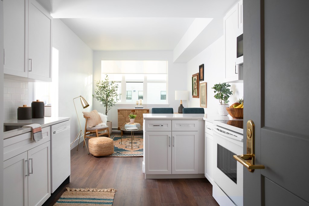 A modern kitchen with white cabinets and a wooden floor.