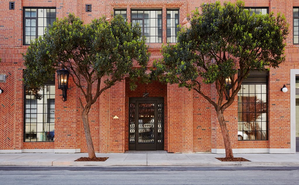 A red brick building with a black door and two trees in front.