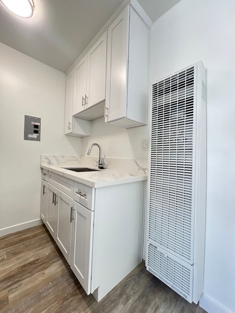 A white kitchen with a sink and a wall-mounted air conditioner.