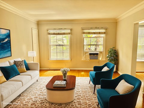 A living room with a white couch, blue armchair, and a coffee table with a vase of flowers on it.