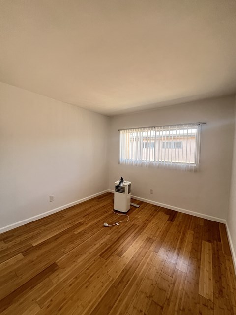 A room with a wood floor and a window with blinds.