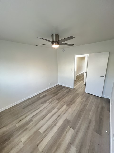 A room with a ceiling fan and light, and a doorway leading to another room.