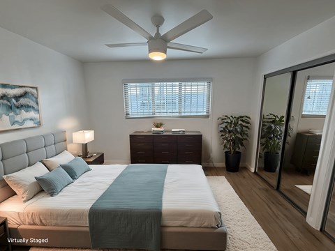 A bedroom with a bed, dresser, mirror, and ceiling fan.