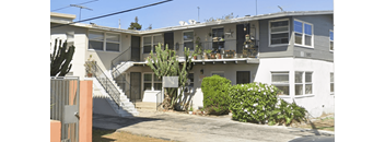 A white two-story house with a balcony and a cactus in front.