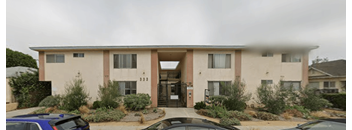 A beige two-story apartment building with a parking lot in front.