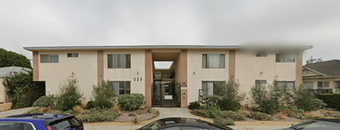 A beige two-story apartment building with a parking lot in front.