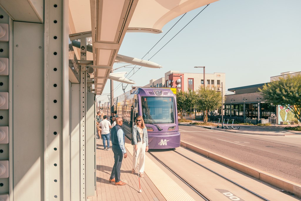 A purple tram is on a track with people waiting to board.