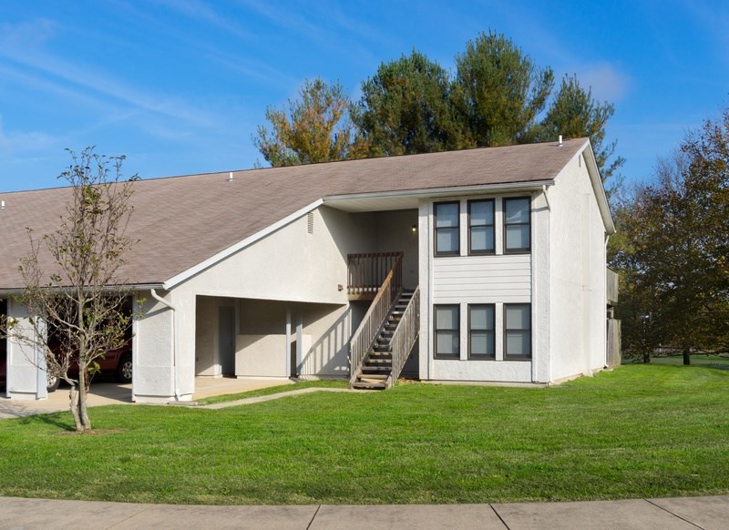 A white house with a brown roof and a tree in front.