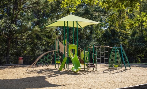 A playground with a green and yellow swing set and a yellow umbrella.