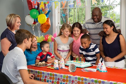 A group of people are gathered around a table with a birthday cake on it.