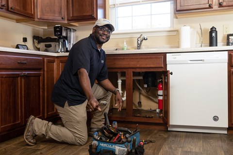A man in a black shirt and khaki pants is kneeling on the floor in front of a washing machine.