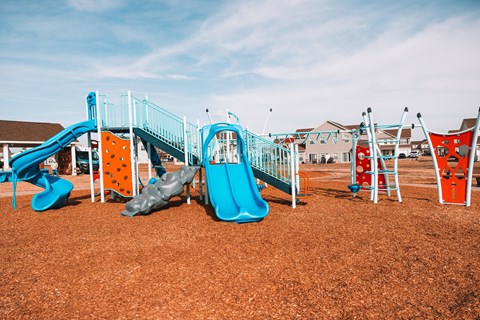 A playground with a blue slide and orange and grey climbing structures.