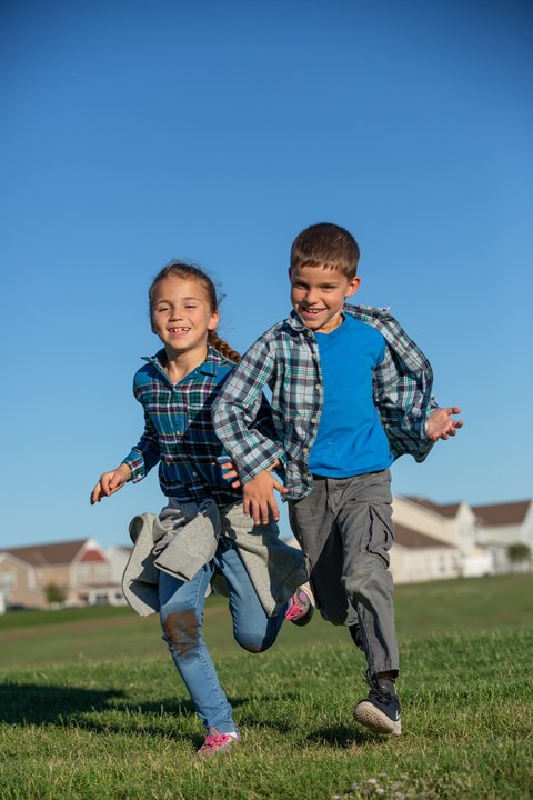 Two children are running in a grassy field.