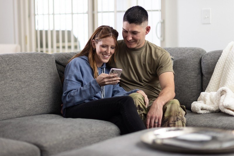 A man and a woman are sitting on a couch, with the woman looking at her phone.