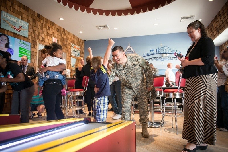 A man in a military uniform is playing a game of bowling with a young girl.