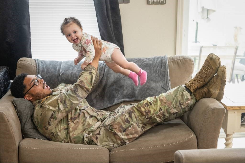 A man in uniform on couch playing with baby girl.