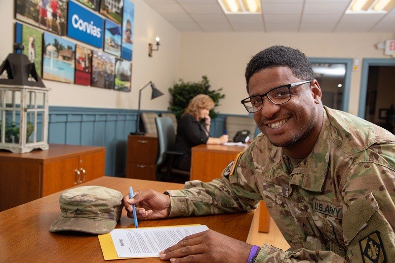 A man in a US Army uniform is signing a document at a desk.